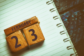 february 23rd. Day 23 of month,Handmade wood cube with date month and day placed on a lined notebook on a blue background. artistic coloring.  winter month, day of the year concept
