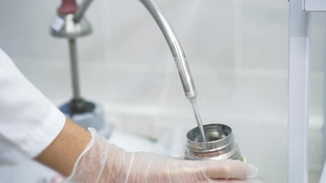 Working with nitrogen gas in medical chemical laboratory. Metal pipe pouring gas looking like dry ice into container. Laboratory assistant works with chemistry