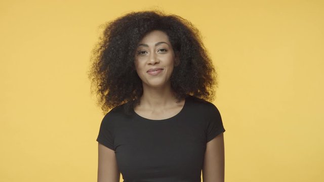 Girl confirm rumors with pleased smile. African-american female with afro hairstyle in black t-shirt, nod in agreement, give positive reply with satisfied smile, talking, agree, yellow background