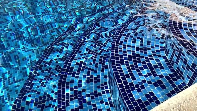 View on pure blue water in the outdoor swimming pool with sunlight reflections. Sunny day, summer mood, wonderful view, breeze. Entrance to the pool, steps into the water. Relax vibes. 