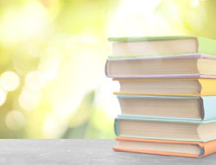 Stack of colorful books on table against blurred green background. Space for text