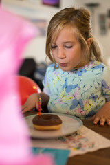 Mädchen im Kleid bläst Kerze auf Doughnut aus - obrazy, fototapety, plakaty