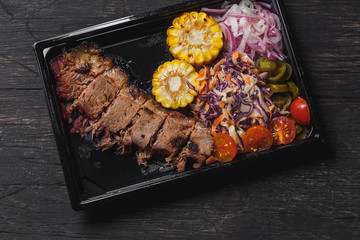 Beef brisket with garnish in plastic black plate
