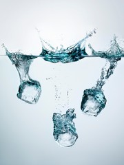 Ice cubes splashing into clear water surface view