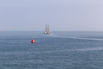 Seascape of sailing ship with sails down off the coast of the UK in the Solent with a red Buoy.