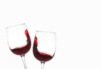 Glasses with red wine and a small splash, waves of wine inside the glass on a white background. Copy space