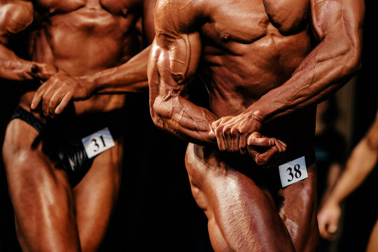 muscular athletic bodybuilder posing biceps on hand in bodybuilding competition