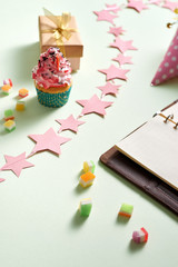 Empty notebook with gift boxes and a cupcake, hat with a candle on light green background, top view