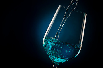 Exotic blue wine, trendy non-classical sweet wine drink pouring into glass on black blue background with copy space