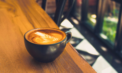 Coffee mug of Latte art coffee breakfast on wood  table  in morning time with light from window  vintage cafe style