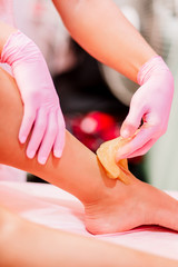 Close-up hands of cosmetologist in rose gloves applying paste for sugaring depilation. A master makes removing unnecessary hair on the legs. Procedure removal in a beauty salon. Depilatory sugar paste