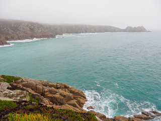 Wide angle view of the rocky shores and calm waters of Porthcuno beach on a foggy day. Cornwall, United Kingdom. Travel and nature. - 310677239