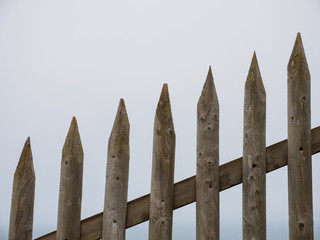 Closeup detail of an old, sloped picket fence along Porthcurno beach on a foggy day. Cornwall, United Kingdom. Nature and generic architecture. - 310677435
