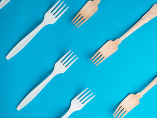 Organic bamboo disposable forks vs plastic ones on trendy blue background. Environmentally friendly wooden and non-oragnic plasticforks