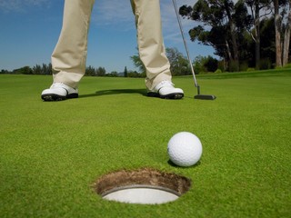Golfer On Green With Ball At Hole In Foreground