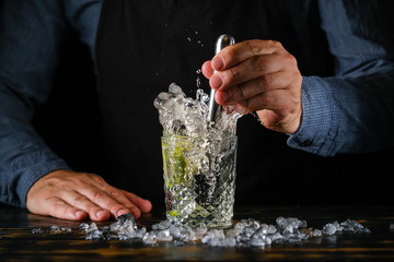 Bartender is preparing a refreshing cocktail with ice and lime. Bartender preparing Caipirinha cocktail. Summer cocktail at the nightclub.