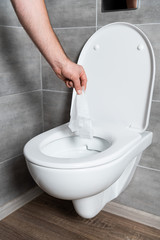 Cropped view of man throwing napkin in clean toilet bowl at bathroom