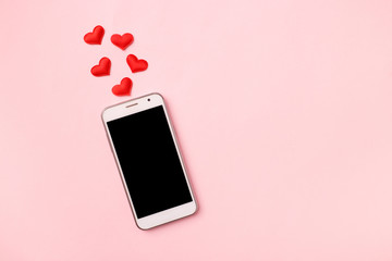 Top view of mobile cellphone and red heart on pink pastel background, copy space. Mockup template for Valentines Day. Love, technology concept. Top view, flat lay.