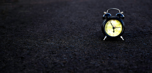 Alarm clock placed on a black brick floor with dark tones.