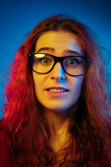 Fototapeta premium Caucasian woman's portrait isolated on blue studio background in neon light. Beautiful female model with red hair in casual style. Concept of human emotions, facial expression, sales, ad. Sad, upset.