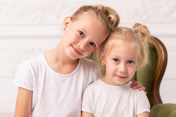Two little blond smiling girls pose for camera while sit in green wooden armchair