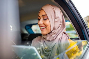 Muslim Businesswoman work with digital tablet computer and holding cup of coffee in back seat of luxury car. Beautiful business woman is using a smart phone while sitting on back seat in the car