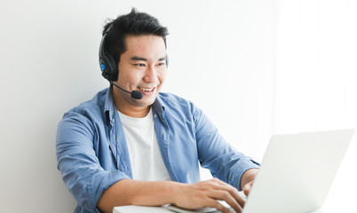 Asian handsome man in blue shirt using laptop with headphone talking smile and happy face - 310682803