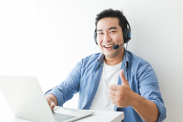 Asian handsome man in blue shirt using laptop with headphone talking smile and happy face