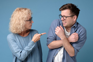 Angry mature woman shouting, blaming millennial annoyed son in eyeglasses. Generation problems. Studio shot