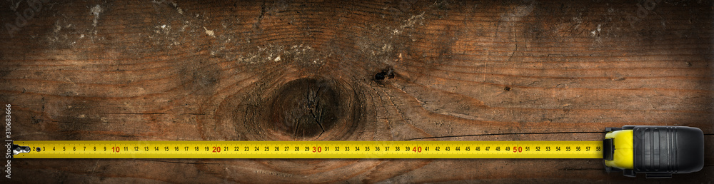 Poster close-up of a yellow and black tape measure on an old work table with copy space and dark shadows