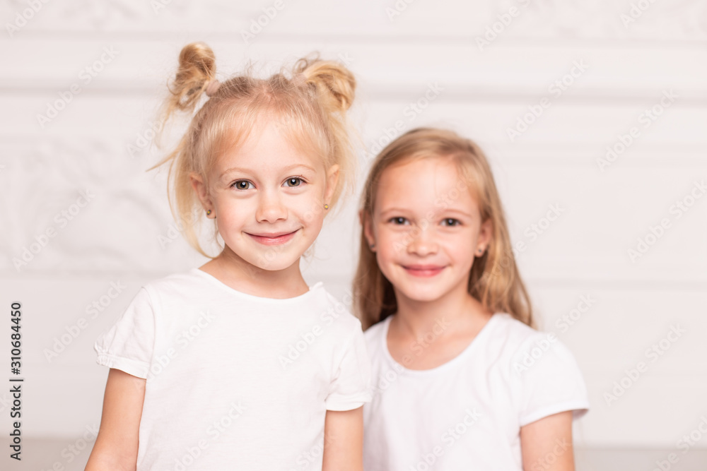 Wall mural two little cute sisters pose for a photo standin next to each other. soft focus