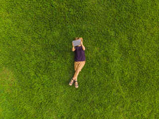 Boy lying on the grass in the park and looks at the tablet. Photos from the drone, quadracopter