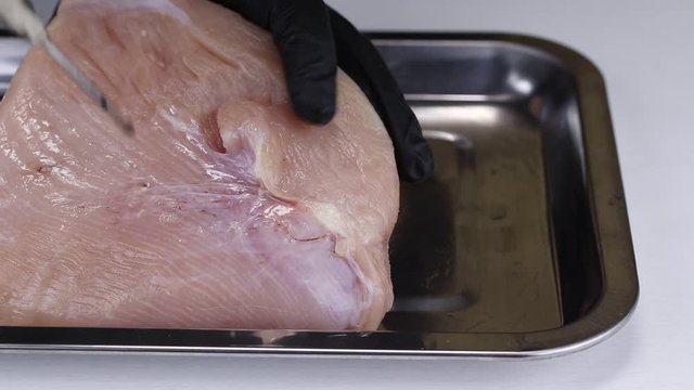 A chef pumps a solution of nitrite salt into a turkey pulp with a syringe and puts it on a metal tray, close-up