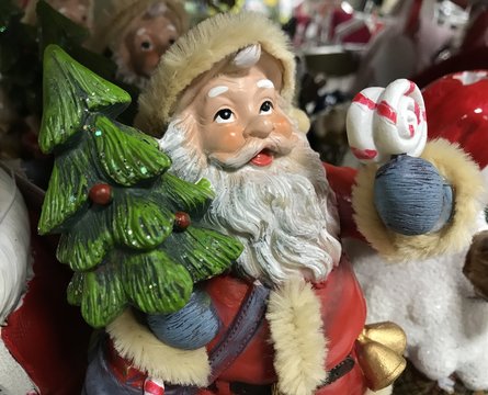 Toy Santa Claus looks up with a Christmas tree in his hands on the background of other toys. Photo with mobile under shop lighting.