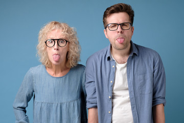 Excited funky funny comic cheerful guy and lady making stick tongue out. Studio shot