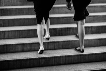 Fototapeta na wymiar Walking upstairs in black and white. Close up legs and shoes of businesswomen walking stepping up stair in the city. Walk together.(motion blurred image) 