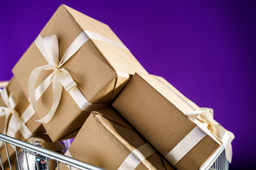 Gifts in craft paper with white tape in a supermarket trolley on a purple background