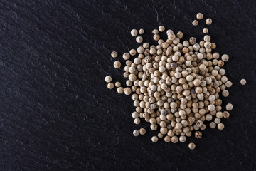 white peppercorns on dark slate stone background