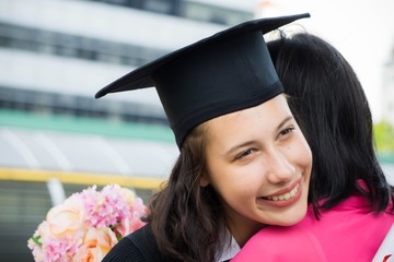 Young beautiful woman graduate hugging her mother at graduation ceremony, University Graduation Certificate Hugging Success Concept