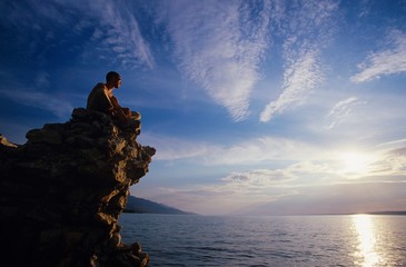 Man Sitting On Rock Overlooking Ocean