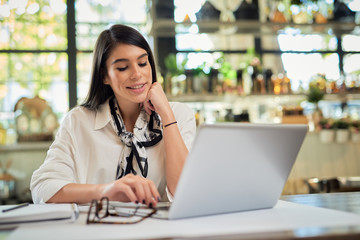 Attractive businesswoman sitting in cafe and using laptop. Hands are on keyboard.