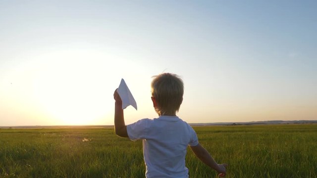 A boy in the field at sunset runs and throws a paper plane. The concept of a happy child