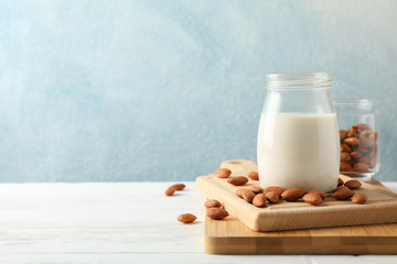 Glass of almond milk, almond seeds on white table again blue background, space for text