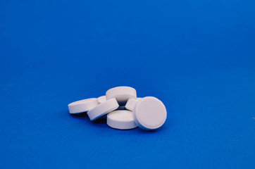 a bunch of white pills lying on a blue background. concept of health and medicine.