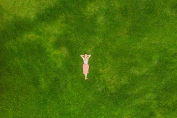 Wallpaper murals Green Young woman lying down in the middle of a field and relaxing, drone photo
