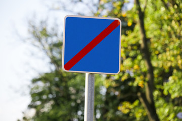 blue red square blank crossed out road sign close up on blurred background of sky and trees