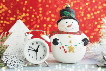 Christmas toy snowman, alarm clock, silver snowflake and tinsel on a red background. Yellow bokeh lights...