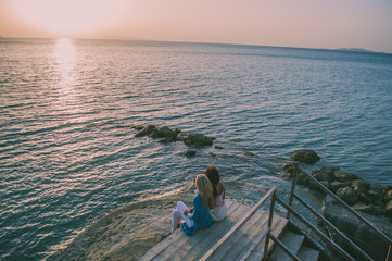 Two girls sitting and waiting for sunset. Blonde and brunette, friends traveling together. Corfu island, Greece.