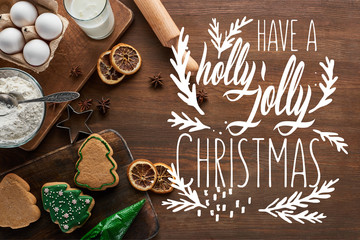 top view of delicious Christmas cookies near ingredients and spices on wooden table with have a holly jolly Christmas lettering