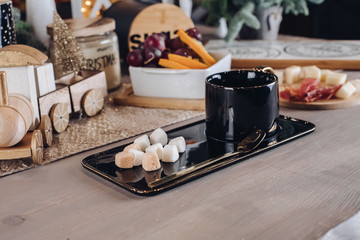 Black ceramic cup on wooden table with food on the background. New Year eve concept